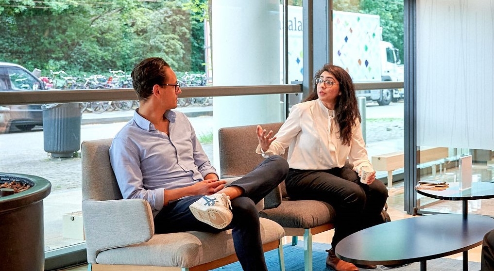 Man and woman sitting on a couch in the office, engaged in conversation.