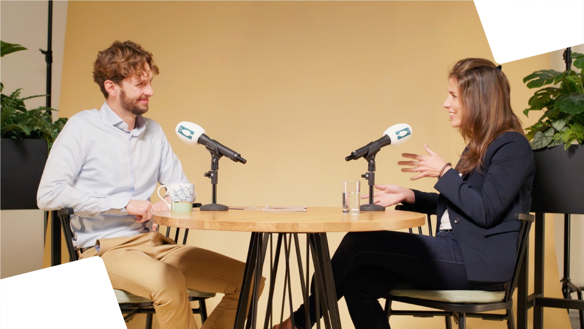 Two people recording a podcast, smiling, with a woman on the right and a man on the left, in a business casual manner. 