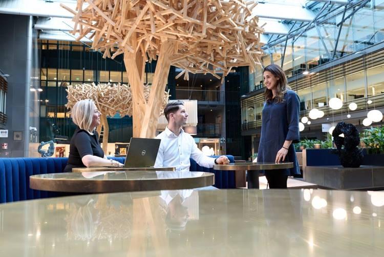 Photo of our office showing three employees together, two of them are working sitting down, but look up as the third comes by